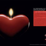 Una candela a forma di cuore con una fiamma accesa. Su fondo nero.